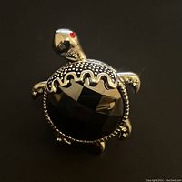 Close-up of black onyx turtle ring showing faceted shell, silver-toned textured turtle body, and red eyes.