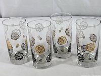 Four clear glass water glasses with chrysanthemum floral designs in white, gold, and black; cylindrical shape; approximately 5-1/2 inches tall