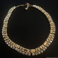 Full view of the gold tone and white rhinestone choker necklace laid out flat to show design and length.