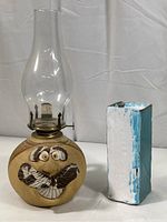 Full view of vintage kerosene oil lamp with goofy face on ceramic base and glazed pottery vase with blue and white colors.