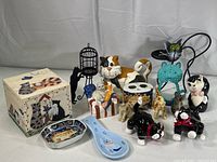 Collection of 15 items including cat figurines, decorative cat box, spoon rest, small skunk figurines, and cat dish.