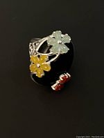 Front angled view showing black onyx center with pale green, yellow, and red flower designs on silver band.