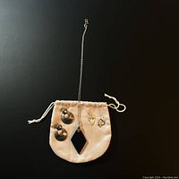 Photo of onyx pendant necklace and two pairs of silver earrings arranged on a small beige drawstring bag on black background.