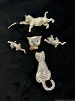 Five vintage silver tone cat brooches displayed on black background, showing full set and details of each piece.