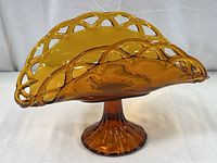 Side angle view of the amber glass pedestal dish showing the lattice rim and flared base