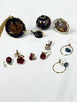 Full lot view showing four Limoges porcelain miniatures including cobalt blue plate, teapot, round vase and white plate with pastoral scene, alongside multiple pieces of vintage jewelry including earrings and pins.