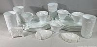 Full set of milk glass pieces displayed on a flat surface, including snack plates, punch cups, milk glasses, tea bag rests, and a card holder, all in white milk glass with grape cluster patterns.