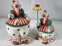 Front view of both clown jars showing size difference, paint details, and missing umbrella on large jar