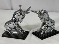 Pair of chrome plated Ronson Art Deco goat ashtray snuffers on black bases, one with lighter inserted, shown from front and side angles.