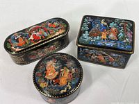 Three vintage Russian Palech ceramic trinket boxes together showing varied shapes and painted fairytale scenes.