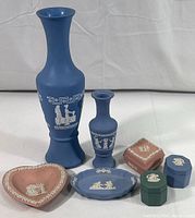 Full view of two blue Wedgwood jasperware vases and five smaller decorative items arranged in front: pink heart dish, blue oval dish, pink diamond box and two small covered ring boxes in green and blue.