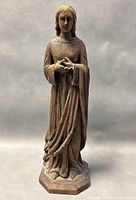 Full front view of a carved wooden religious figure standing with hands positioned in front, wearing detailed flowing robes and standing on a hexagonal base.