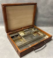 Open walnut painter's box showing metal compartments inside, likely for paint tubes and brushes.