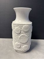 Front view of white porcelain vase showing textured bas-relief concentric circle design on roughened surface.