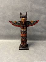 Front view of the hand carved and painted First Nation totem pole showing detailed faces and wings with vibrant colors.
