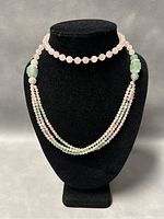 Front display of the necklace on a black stand showing round beads and layered strands.