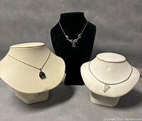 Three sterling silver necklaces displayed on necklace stands, varying designs and lengths visible.