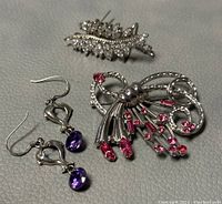 Top view of entire jewelry set including two brooches and one pair of earrings with purple crystals and hooks