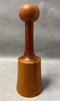 Full view of the teak pepper mill upright showing the rounded top knob, slender neck, and solid base