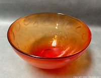 View of the translucent orange blown glass bowl showing the interior decorative rounded indentations and gradient color effect.