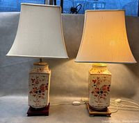 Pair of Chinese porcelain crackle glaze lamps with floral decorations and fabric shades, shown side by side on a surface with visible cords and stands.