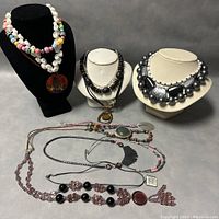Photo of six assorted vintage costume necklaces posed on black and white jewelry displays and flat surface.