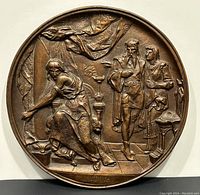 Front view of the round bronze plaque showing the Macbeth scene with three figures and detailed background.