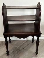 Front view of the antique dark wood 3 tier side table showing overall structure and condition.