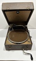 Front view of the open suitcase gramophone showing the turntable, tonearm, and hand crank.