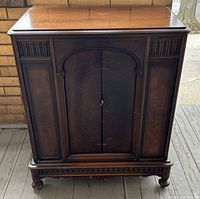 Front view of antique wooden smokers cabinet with closed double doors and carved details on the front panels and legs.