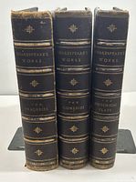 Three volumes upright showing spines titled 'Shakespeare's Works', 'The Tragedies', 'The Comedies', 'The Historical Plays' with gilt decoration on dark leather.