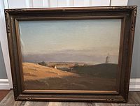 Full view of framed landscape painting showing gold-tone decorative frame and rural scene with sailboat on horizon.