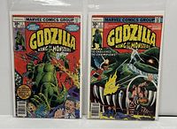Two Godzilla King of Monsters comics side by side in protective sleeves with bag and board.