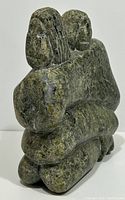 Front angle view of the Inuit soapstone carving showing the mother and child figures embracing, highlighting texture and color of the greenish stone.