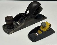 Two vintage metal wood planes, larger National brand with front wooden knob and curved handle, and smaller black and yellow miniature trimming plane.