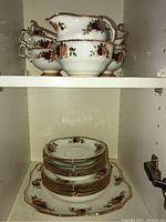 Photo showing six floral-patterned teacups stacked with one creamer and sugar bowl on top shelf, plates on bottom shelf