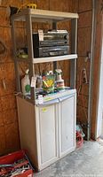 Full view of white plastic storage cabinet with three open shelves above and cupboard below, placed in garage setting.