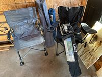 Five folding outdoor chairs including one Roots arm chair with footrest, two gray fabric folding chairs, and two other folding chairs, all in a garage setting.