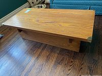 Angled view of the oak coffee table placed on wood flooring with visible brass corner details.