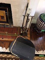 Photo of fireplace tool set including stand and four metal tools positioned upright against wall near fireplace, showing rust and wear.