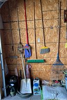 Garden tools including brooms, shovels, rakes, a container of garden crystals, and bag of soil in garage corner