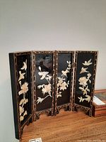 Full front view of black lacquered 4-panel decorative screen showing ivory-colored bird and floral inlays and gold decorative border pattern.