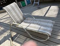 View of the lounge chair from a front angle showing the fabric and metal frame on a wooden deck with shadows.