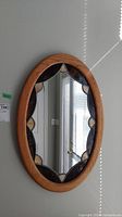 Oval oak frame mirror hanging on wall with slag glass style accents on inner border, clear reflective surface.