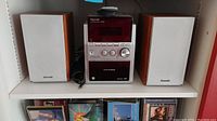 Panasonic stereo main control unit with two wooden speakers on white shelving, CD changer and multiple control knobs visible.