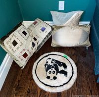 Set of four pillows on hardwood floor corner with teal walls, including two patchwork embroidered square pillows, one shiny rectangular pillow, one plain cream pillow, and round panda mat