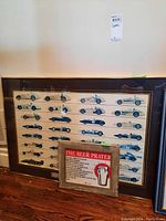 Two framed posters on the floor. Large World Driving Champions poster showing racing cars and smaller Beer Prayer poster in front.