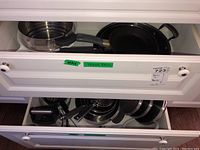 Drawer with various pots and pans, including stainless steel and black frying pan