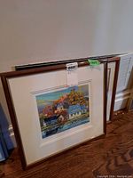 Two framed prints leaning against a wall showing colorful village waterfront scenes.