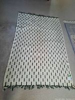 Photo showing the entire rectangular cotton rug with a white base and dark short vertical lines, fringes visible at one end